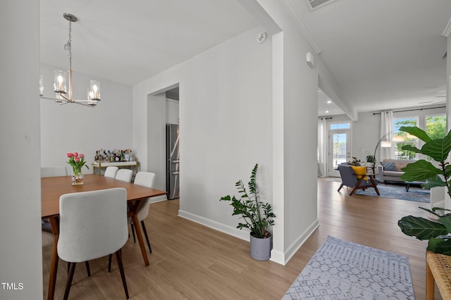 dining room featuring baseboards, visible vents, light wood-type flooring, and a chandelier
