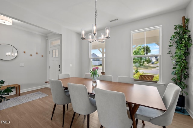dining area featuring an inviting chandelier, baseboards, light wood-type flooring, visible vents, and ornamental molding