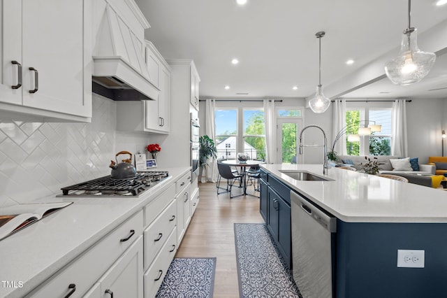 kitchen with premium range hood, blue cabinets, a sink, appliances with stainless steel finishes, and backsplash