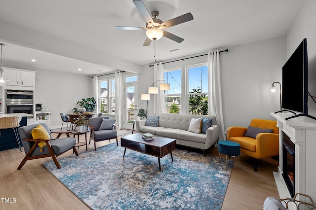 living room with a fireplace, light wood-style flooring, a ceiling fan, baseboards, and recessed lighting