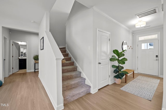 entrance foyer featuring crown molding, light wood finished floors, stairs, and visible vents