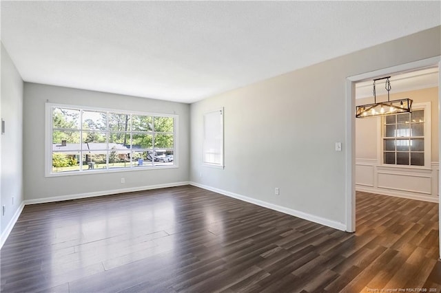 unfurnished room with baseboards, dark wood-style floors, and an inviting chandelier
