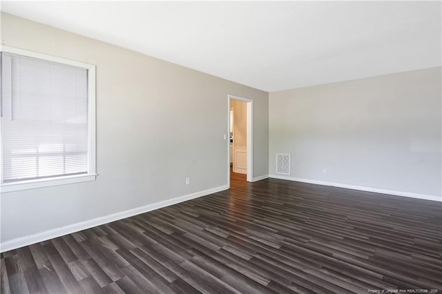 spare room featuring baseboards, visible vents, and dark wood finished floors
