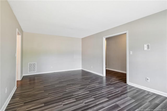 empty room featuring dark wood-type flooring, visible vents, and baseboards