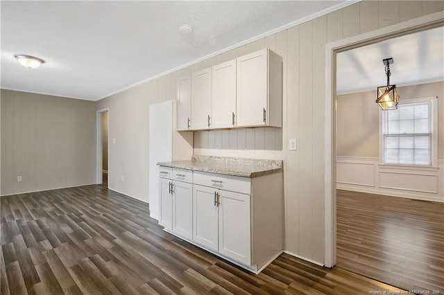 kitchen with white cabinets, dark wood-style floors, light stone counters, a decorative wall, and ornamental molding