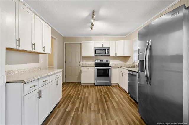 kitchen featuring stainless steel appliances, a sink, a textured ceiling, white cabinetry, and crown molding