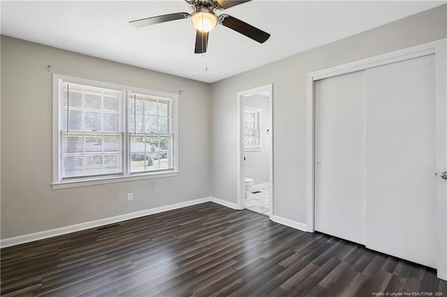 unfurnished bedroom with a closet, ceiling fan, baseboards, ensuite bath, and dark wood-type flooring