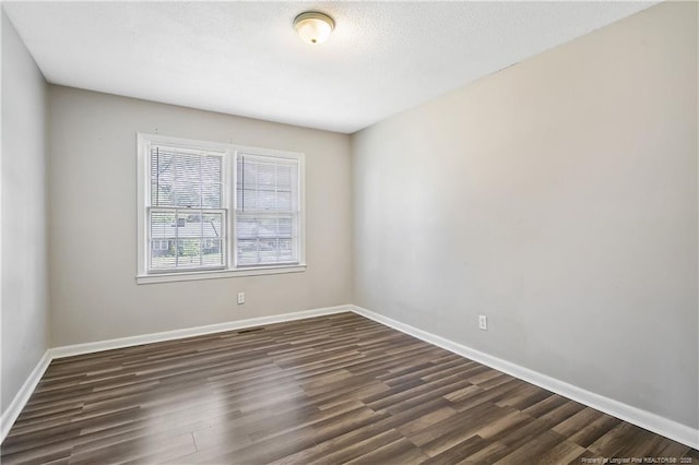 spare room featuring baseboards and dark wood-type flooring