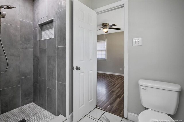 bathroom featuring a tile shower, marble finish floor, toilet, baseboards, and ceiling fan