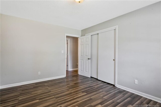 unfurnished bedroom featuring baseboards, dark wood-type flooring, and a closet