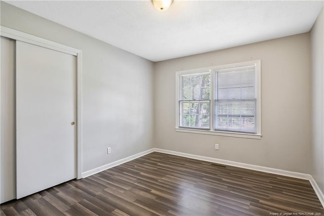 unfurnished bedroom with baseboards, a closet, and dark wood-style flooring