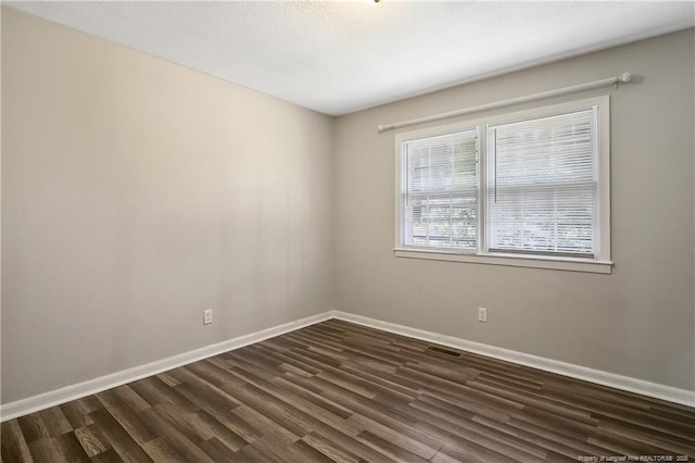 unfurnished room featuring visible vents, baseboards, and dark wood-style floors