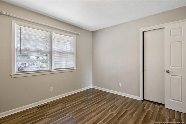 unfurnished bedroom with baseboards, dark wood-type flooring, visible vents, and a closet