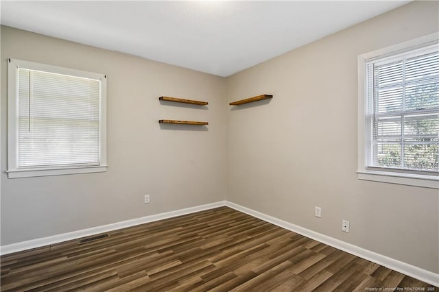 empty room featuring dark wood finished floors, visible vents, and baseboards