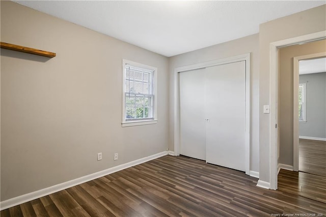unfurnished bedroom with baseboards, dark wood finished floors, a closet, and multiple windows
