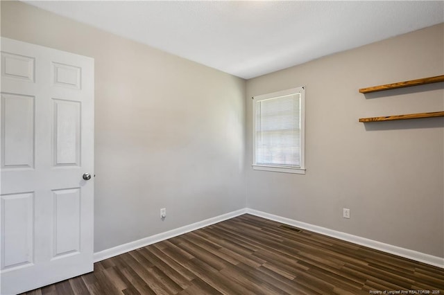 spare room featuring baseboards, visible vents, and dark wood-style floors