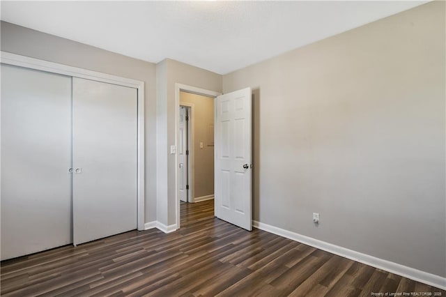 unfurnished bedroom with dark wood finished floors, a closet, and baseboards