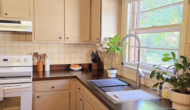 kitchen with under cabinet range hood, white range with electric stovetop, backsplash, dark countertops, and a sink