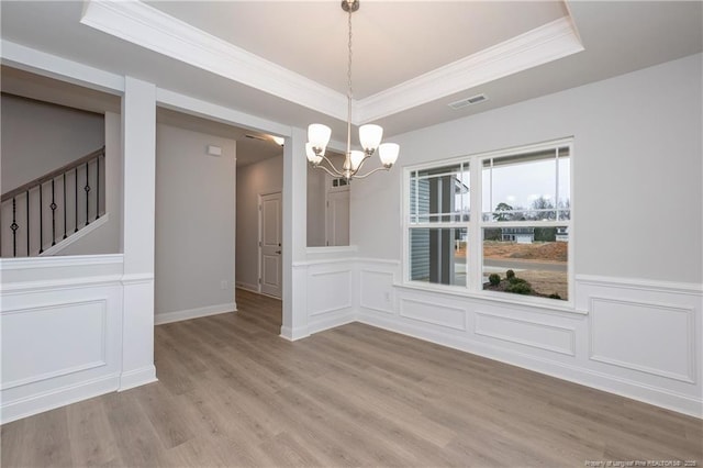unfurnished dining area featuring a decorative wall, a chandelier, light wood-style flooring, a tray ceiling, and visible vents
