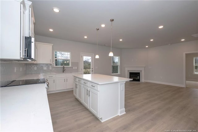 kitchen featuring a kitchen island, stovetop, tasteful backsplash, a sink, and white cabinets