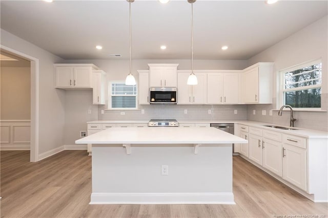 kitchen featuring white cabinets, a sink, range, stainless steel microwave, and a kitchen island