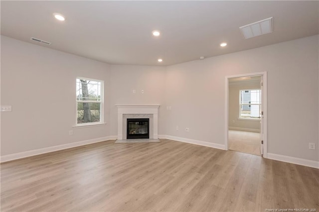 unfurnished living room featuring visible vents, a high end fireplace, light wood finished floors, and baseboards