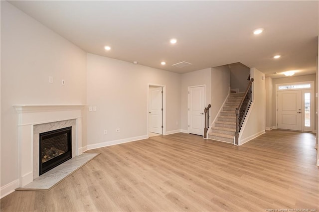 unfurnished living room with a fireplace, stairs, recessed lighting, baseboards, and light wood-type flooring