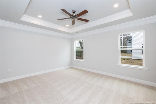 empty room with ornamental molding, a ceiling fan, a tray ceiling, and light carpet