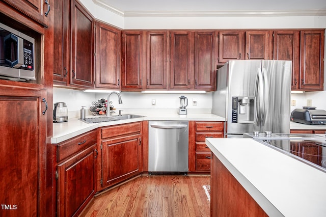 kitchen with light wood-style flooring, stainless steel appliances, light countertops, and a sink