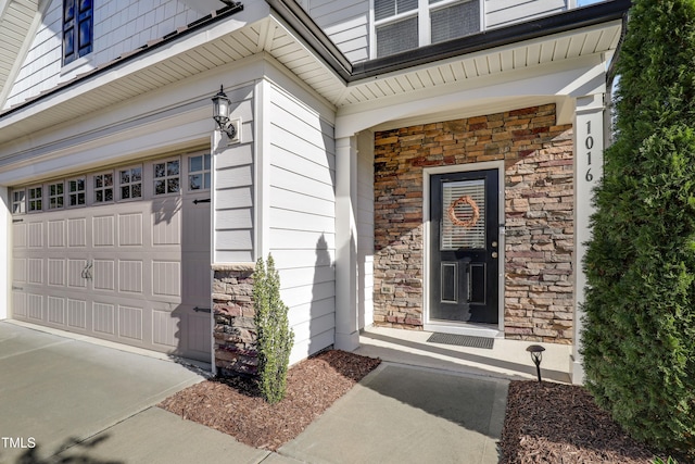 doorway to property featuring concrete driveway, an attached garage, and stone siding