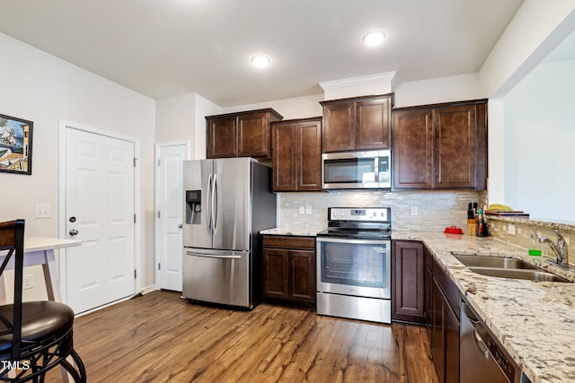 kitchen with light stone counters, a sink, dark brown cabinetry, stainless steel appliances, and dark wood-type flooring