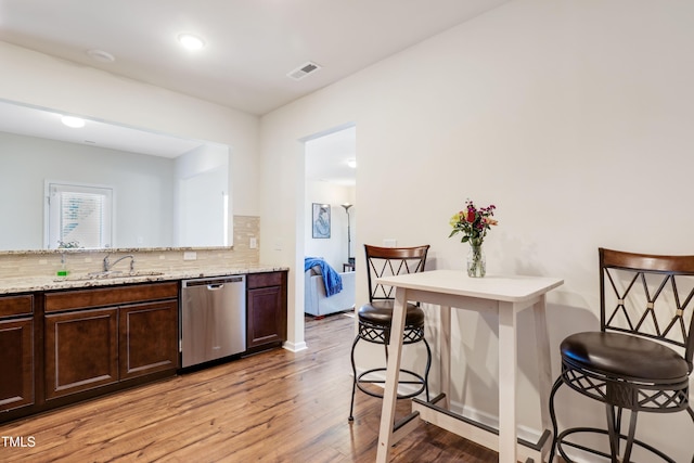 kitchen featuring a breakfast bar, dark brown cabinets, visible vents, stainless steel dishwasher, and light wood-style floors