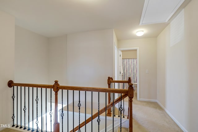 corridor featuring light colored carpet, attic access, baseboards, and an upstairs landing