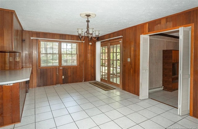 unfurnished dining area with an inviting chandelier, a textured ceiling, and wooden walls
