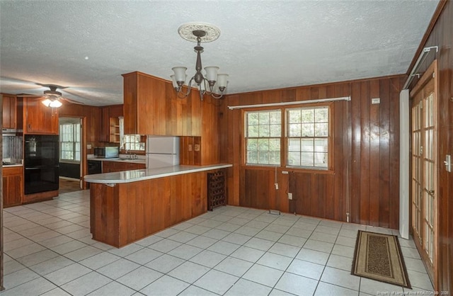 kitchen featuring a peninsula, plenty of natural light, freestanding refrigerator, brown cabinets, and light countertops