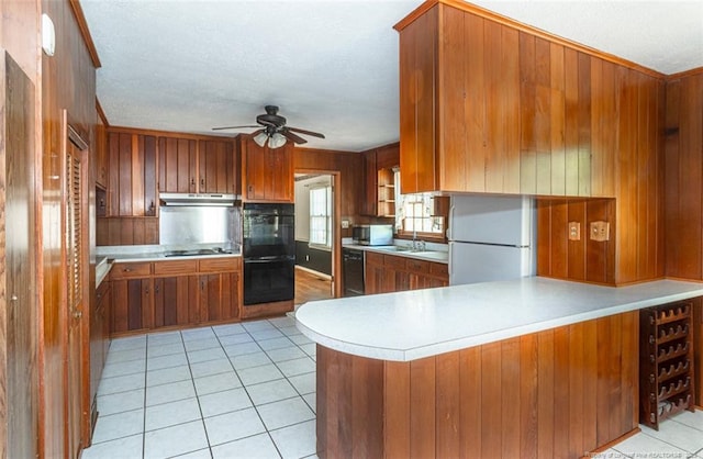 kitchen featuring light countertops, brown cabinetry, under cabinet range hood, and black appliances