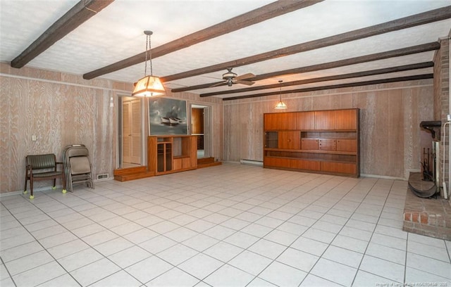 unfurnished living room with visible vents, beamed ceiling, baseboard heating, wood walls, and ceiling fan