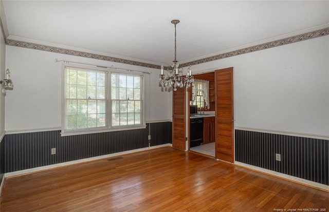 unfurnished dining area featuring wainscoting, wood finished floors, a chandelier, and crown molding