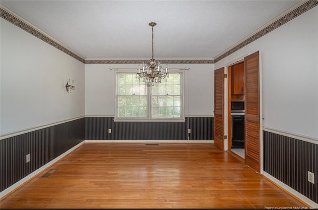 unfurnished dining area with a chandelier, light wood-style floors, a wainscoted wall, ornamental molding, and visible vents