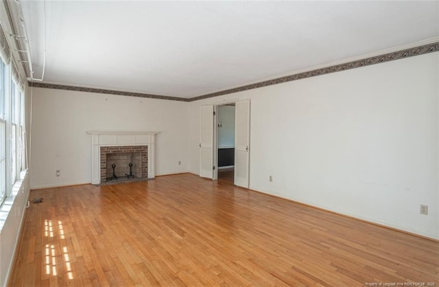 unfurnished living room featuring baseboards, ornamental molding, a brick fireplace, and light wood-style floors