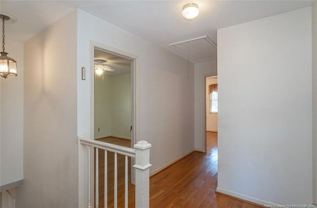 corridor with attic access, wood finished floors, baseboards, and an upstairs landing