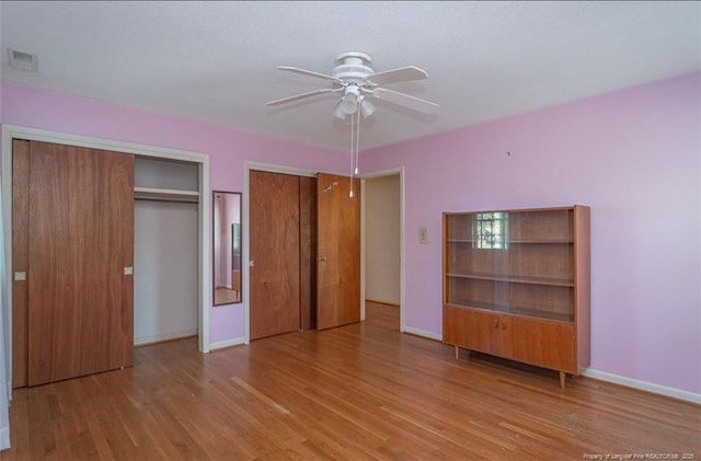 unfurnished bedroom with two closets, visible vents, baseboards, and wood finished floors