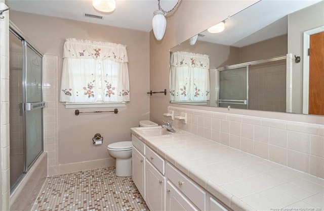 full bathroom with combined bath / shower with glass door, vanity, backsplash, toilet, and tile patterned flooring