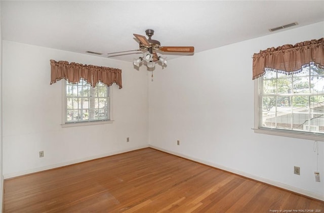 empty room featuring plenty of natural light, wood finished floors, visible vents, and ceiling fan