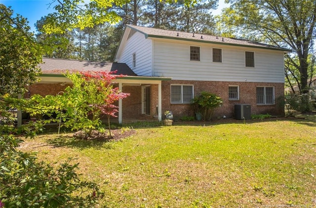 back of property with central AC unit, brick siding, and a yard