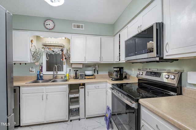 kitchen featuring visible vents, marble finish floor, white cabinets, a sink, and appliances with stainless steel finishes