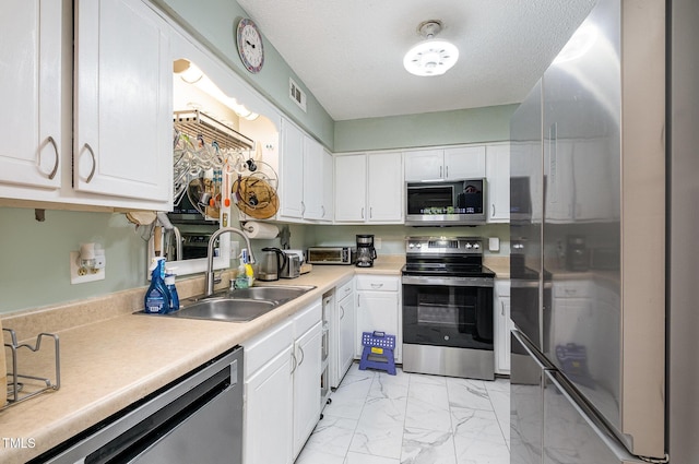 kitchen featuring a sink, stainless steel appliances, white cabinetry, and marble finish floor
