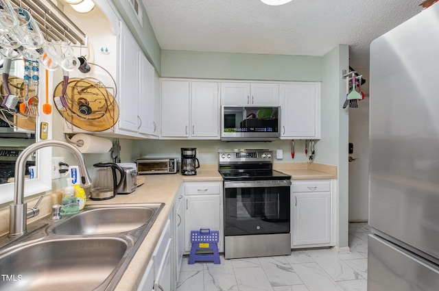 kitchen with white cabinets, appliances with stainless steel finishes, a sink, light countertops, and marble finish floor