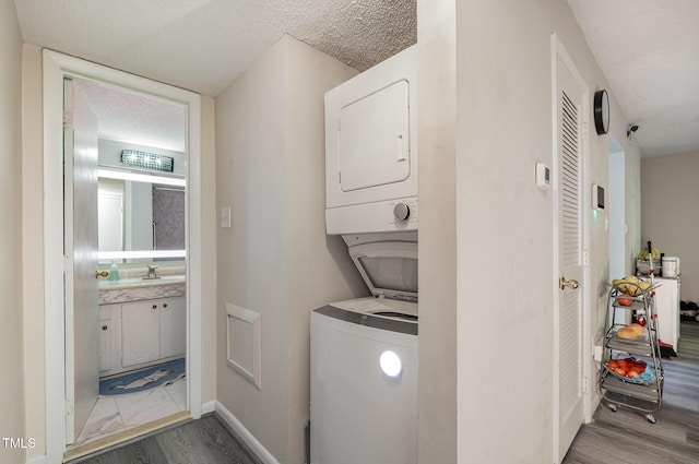 washroom featuring laundry area, a sink, wood finished floors, and stacked washer / dryer