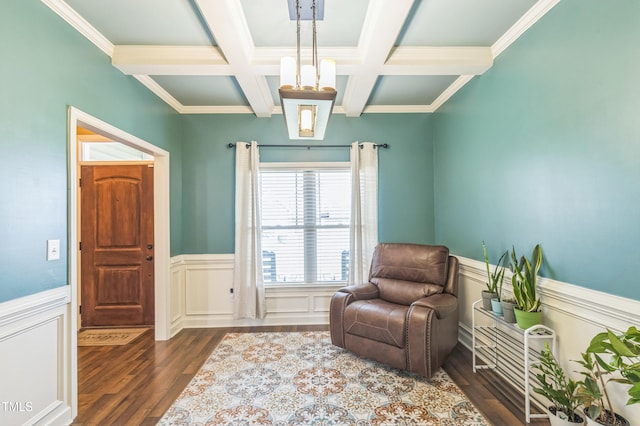 sitting room featuring wood finished floors, a wainscoted wall, coffered ceiling, ornamental molding, and beam ceiling